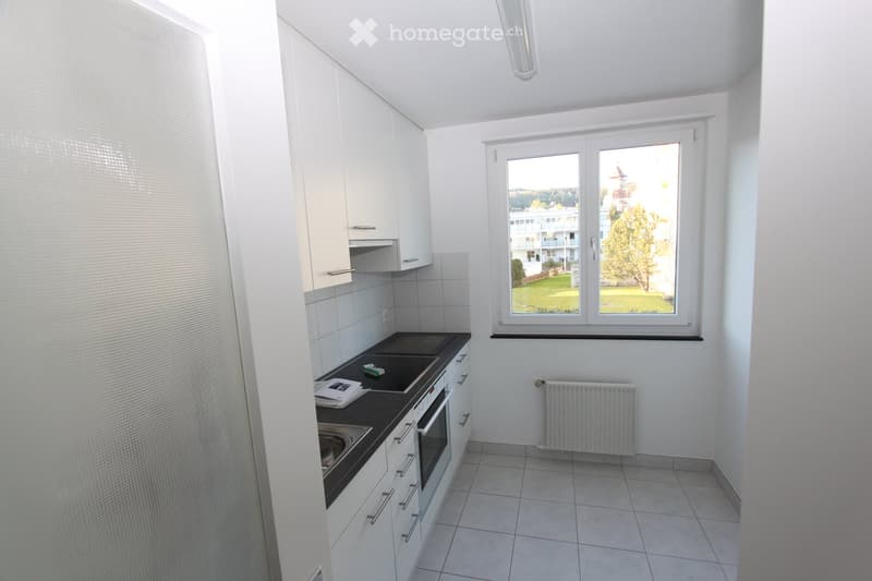 Modern kitchen with white cabinets, tiled floor, and a window overlooking a green area.