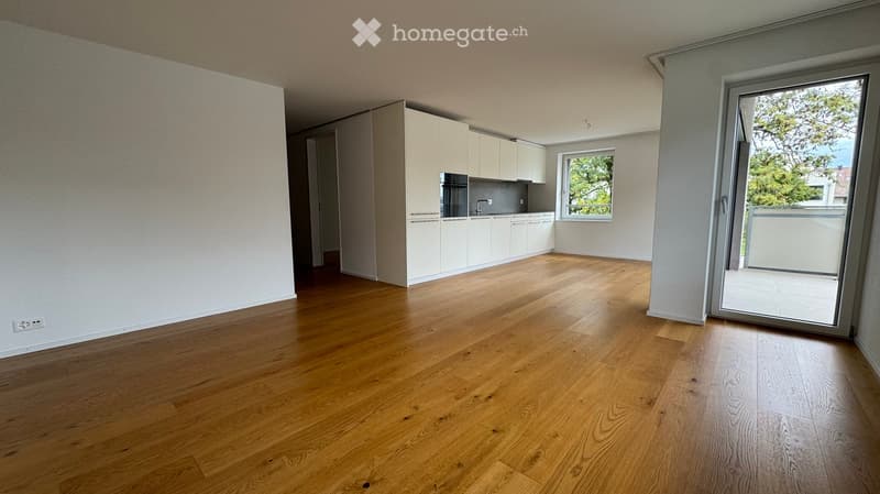 Empty room with wooden flooring, white cabinetry, and a large window with a view of greenery. The room is unfurnished and has a modern, minimalist design.