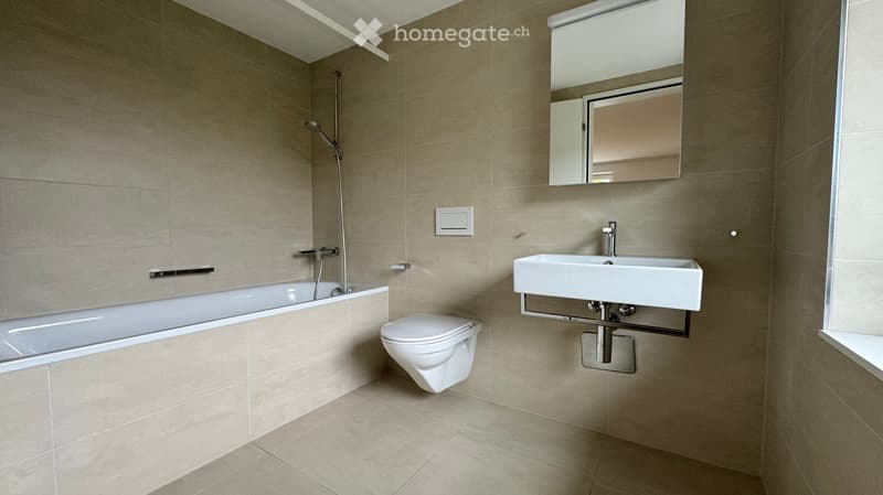 Modern bathroom with beige tiles, a bathtub, toilet, sink, and a mirror above the sink.