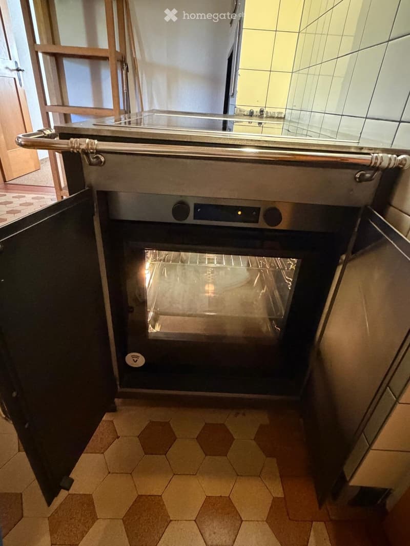 Modern kitchen with a built-in oven featuring a stainless steel finish and glass door, hexagonal tile flooring, and adjacent cabinetry.