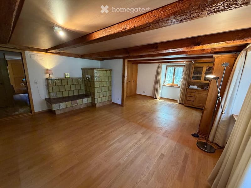 Spacious room with wooden floors, exposed wooden beams, fireplace, cabinet, and large window with curtains.