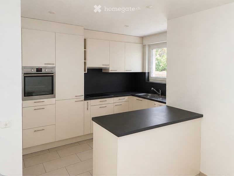 Modern kitchen with white cabinets, black countertops, and stainless steel appliances including an oven and sink.