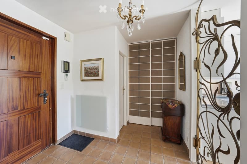 Elegant hallway with wooden doors, a chandelier, a framed picture, and a small wooden console table with a decorative cloth on top.
