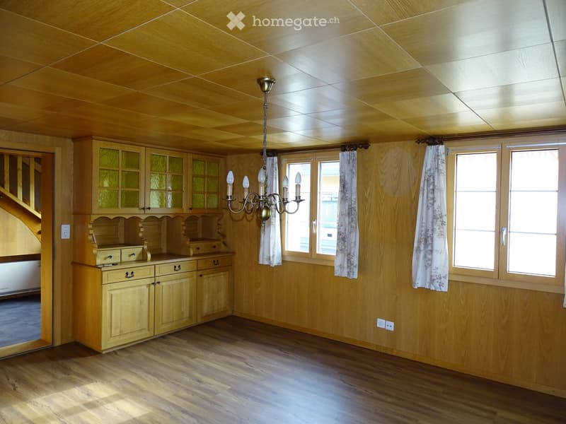 Empty room with wooden walls, ceiling, and flooring, featuring built-in cabinets, a chandelier, and large windows with curtains.