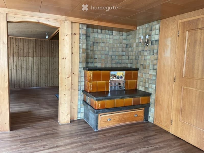 Empty room with wooden flooring, exposed wooden beams, and a tiled fireplace area.