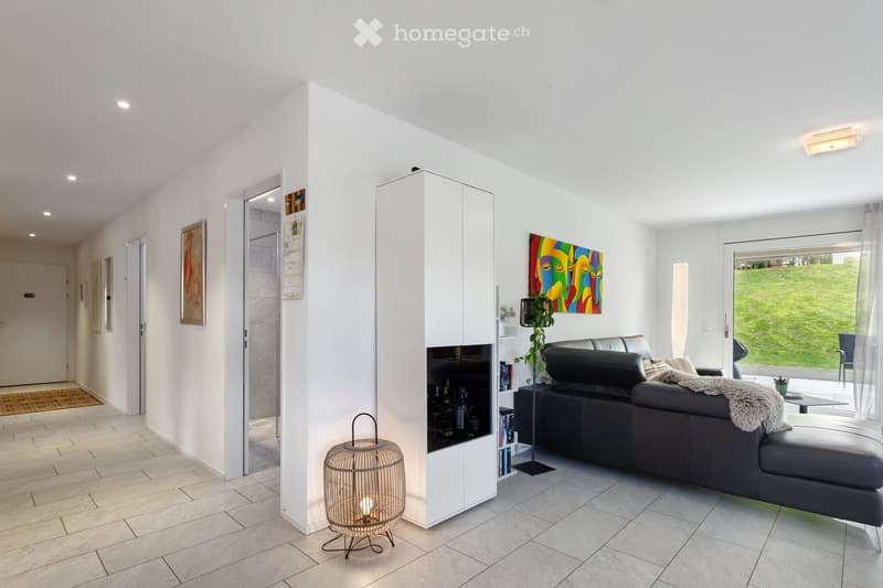 Modern living room with white walls, grey sofa, coffee table, floor lamp, cabinet, and artwork on the wall.