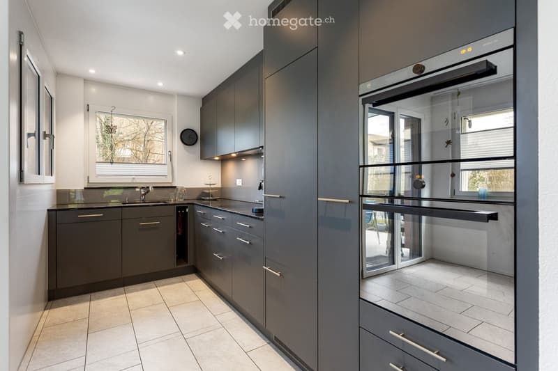 Modern kitchen with dark grey cabinets, stainless steel appliances, and a large window overlooking the garden.