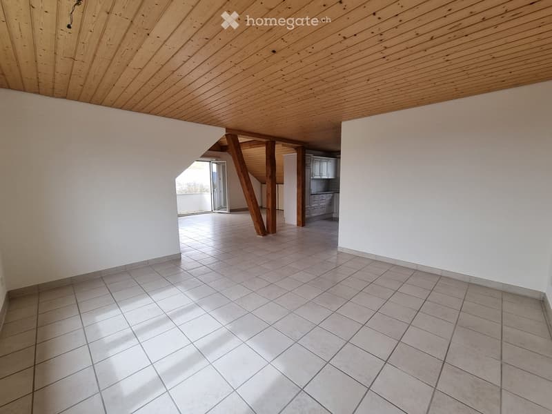 Empty room with wooden ceiling, tiled floor, white walls, open door leading to balcony, a kitchen visible at the back with cabinets and drawers