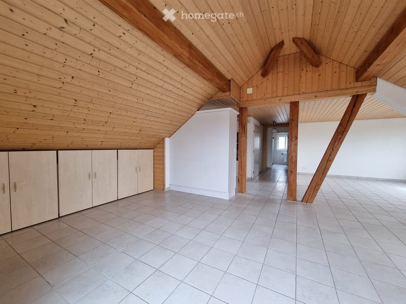 Empty attic room, white tiles, wooden beam ceiling, cabinets on left, white wall on right, doorway leading to another room
