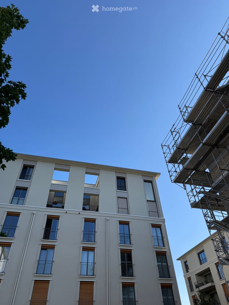 Modern multi-story residential building with large windows, balconies, and a clean facade. The building has a contemporary design with visible balconies and a clear sky background.