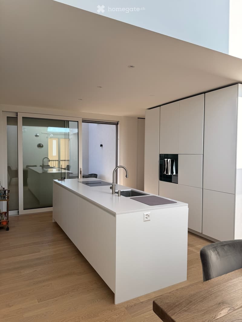Modern kitchen with white cabinetry, a central island with a sink and faucet, and an oven built into the cabinetry. The space features wooden flooring and large glass doors leading to another room.