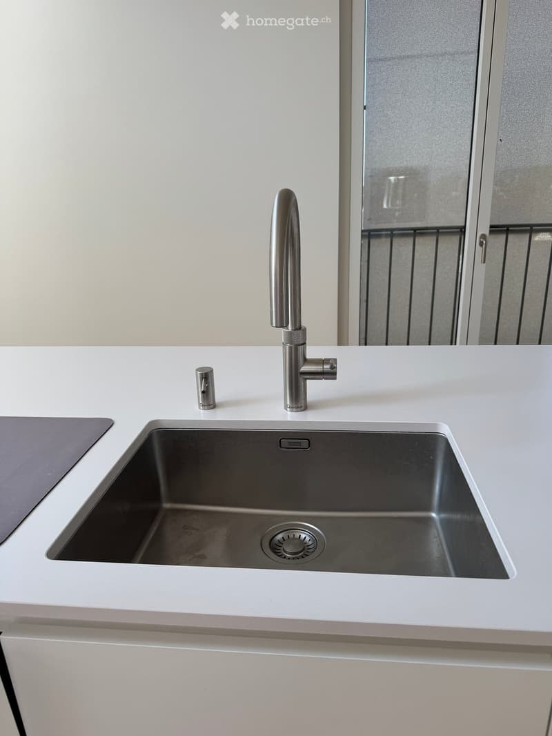 Modern kitchen sink with a sleek stainless steel faucet and a single-basin sink, set into a white countertop.