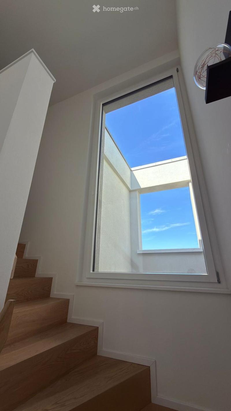 Staircase with wooden steps and white walls, featuring a large skylight window offering a view of the clear blue sky.