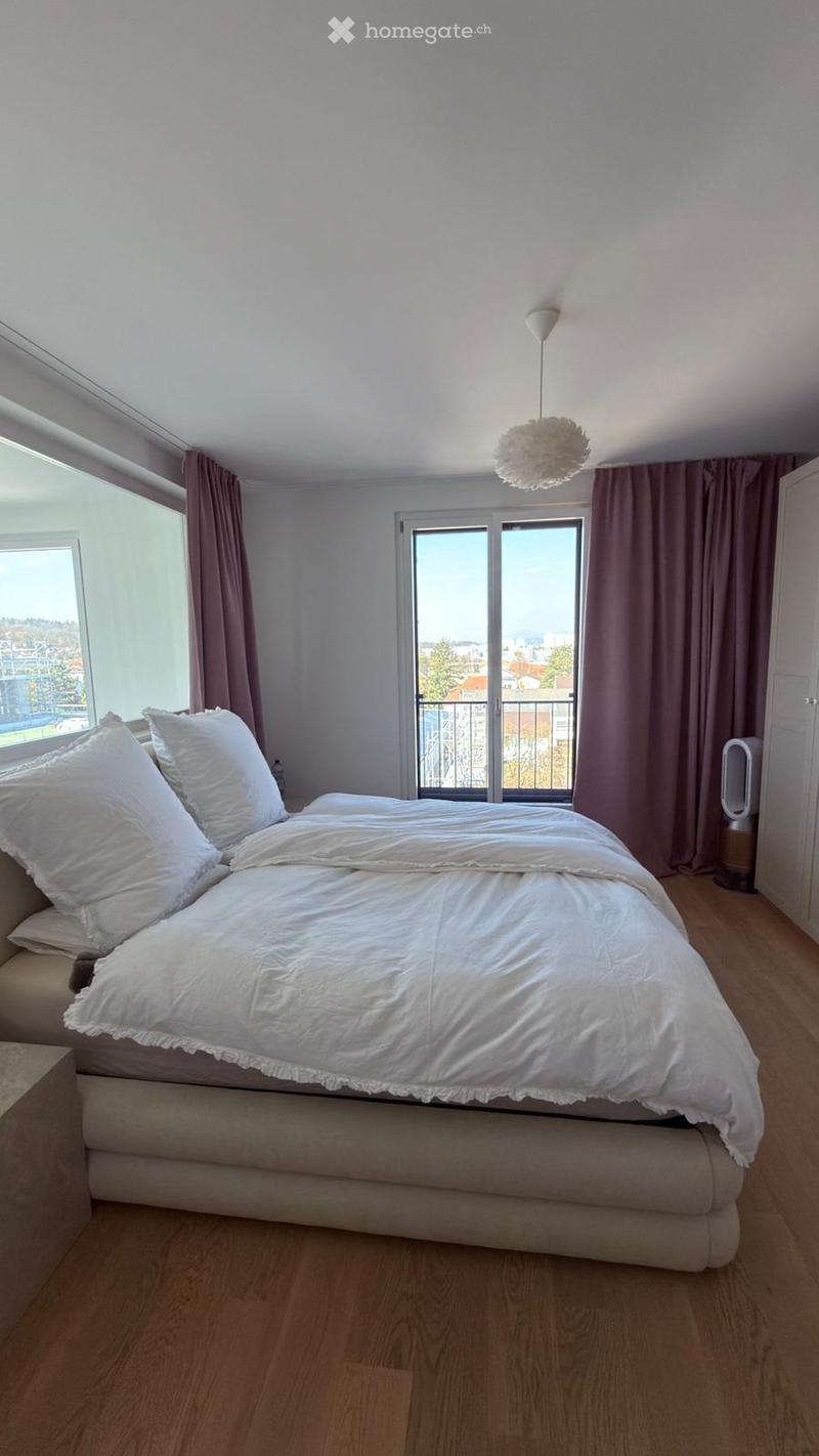 Modern bedroom with a large bed, white bedding, and pillows, large windows with curtains, and a hanging decorative lamp.