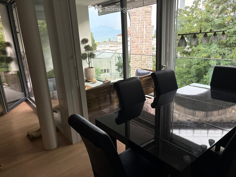 Modern dining area with a sleek black glass dining table, four black chairs, and a potted plant on the balcony.