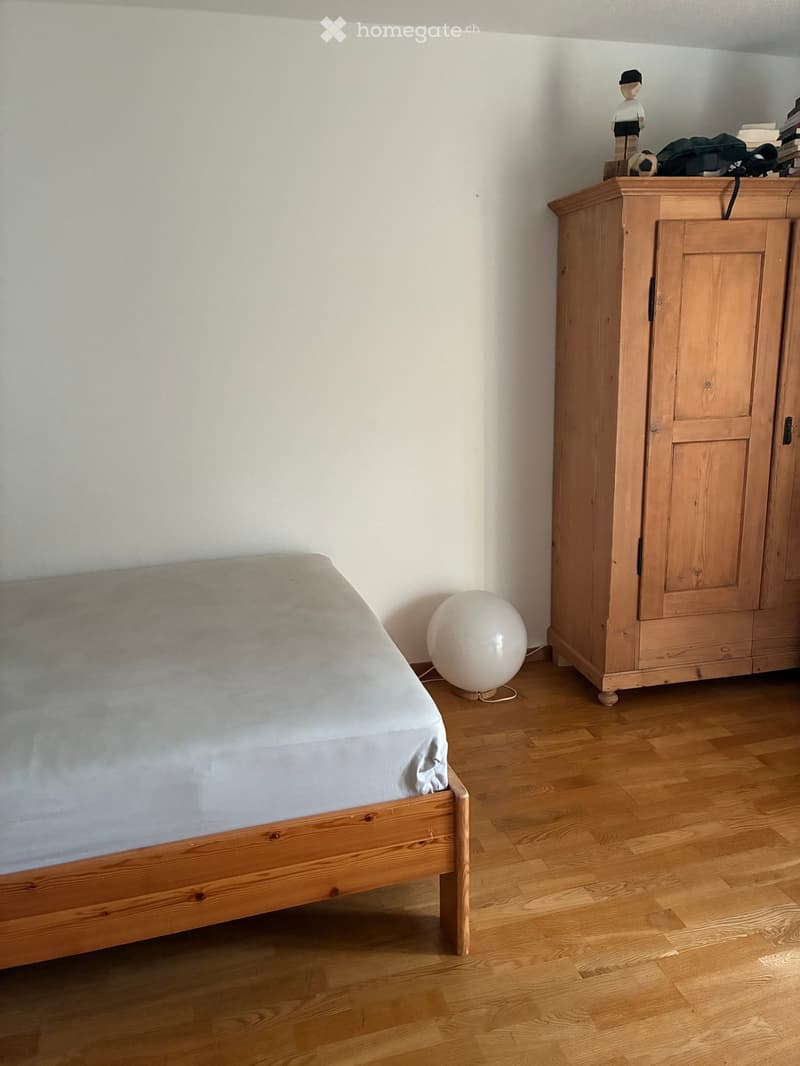 A simple bedroom with a wooden bed, a wardrobe, and a round white lamp on the floor.