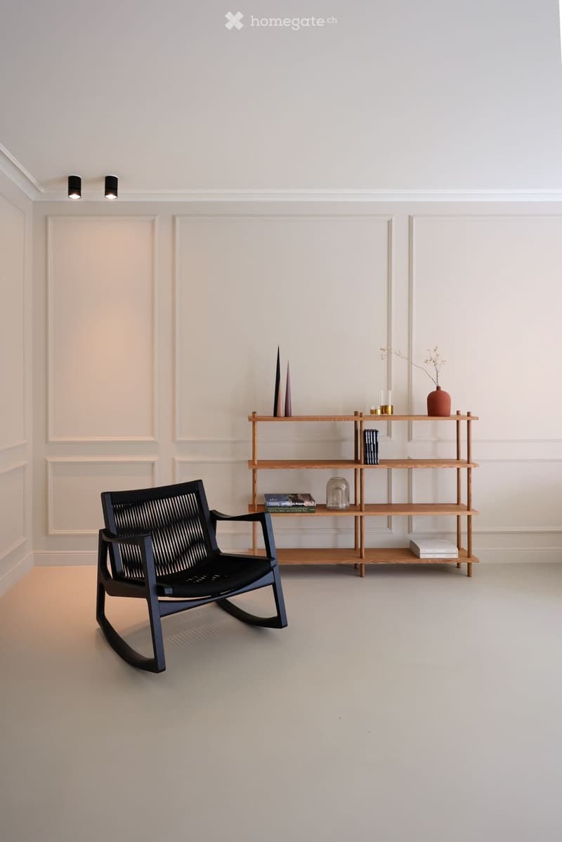 Minimalist room with white walls, black rocking chair, wooden shelf with books and decorative items