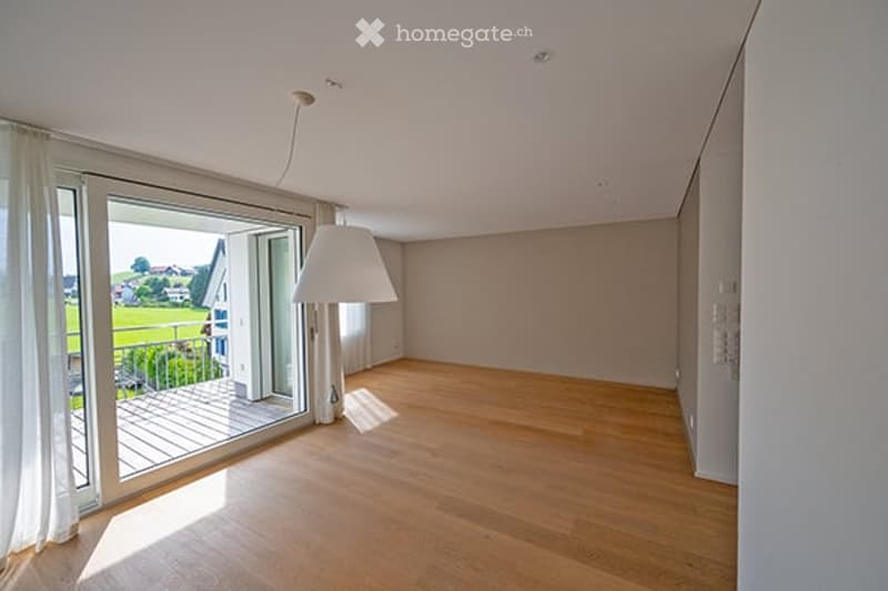 Empty room with wooden flooring, large window leading to a balcony, white walls, and a modern light fixture.