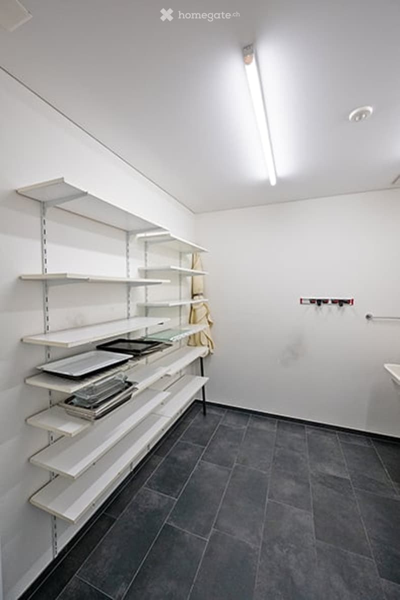Empty room with white walls, dark grey tiled floor, and white shelving unit with several empty shelves.