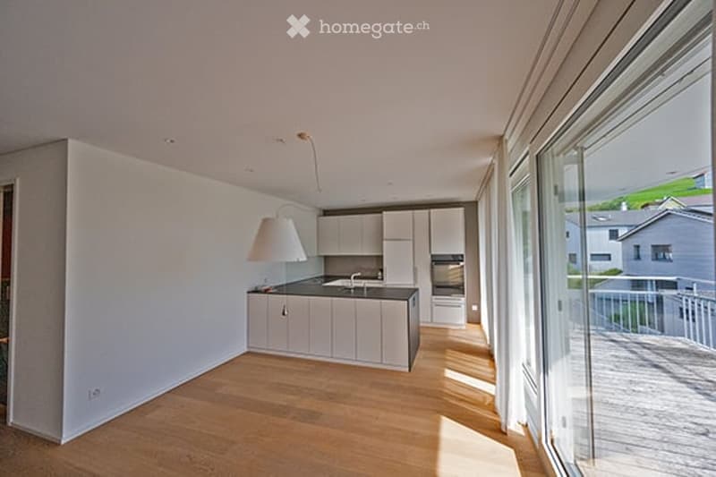 Modern, minimalist kitchen with white cabinets, black countertops, and a large window offering a scenic view. Features include a pendant light, sink, and oven.