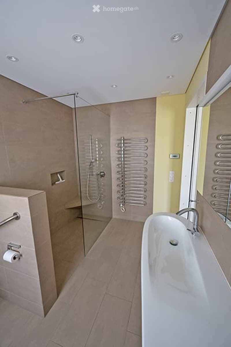 Modern bathroom with a large bathtub, glass-enclosed shower, and multiple radiators for heating.