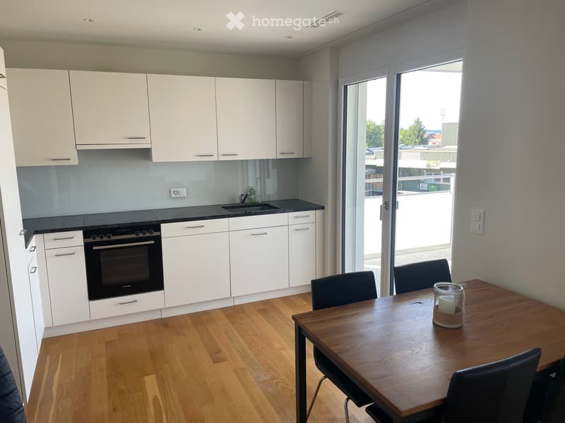 Modern kitchen with white cabinets, black countertops, and a wooden dining table with chairs. Features an oven, sink, and candle on the table.