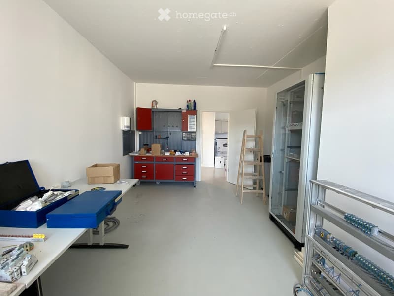 Workshop or storage area with a table, cabinets, ladder, shelves, and various tools and boxes.