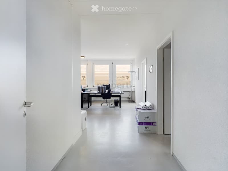Bright, minimalist hallway leading to a furnished room with a desk, chair, books, and storage boxes.