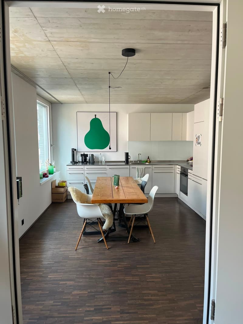 Modern kitchen with white cabinets, wooden dining table, white chairs, and various kitchen appliances.
