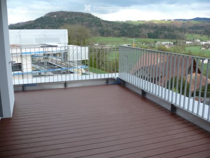Balcony with wooden decking, metal railing, and scenic view of hills and countryside.