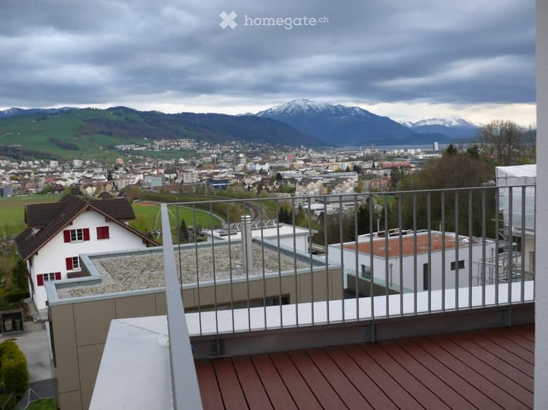 Balcony with wooden decking, metal railing, overlooking a cityscape and mountains.