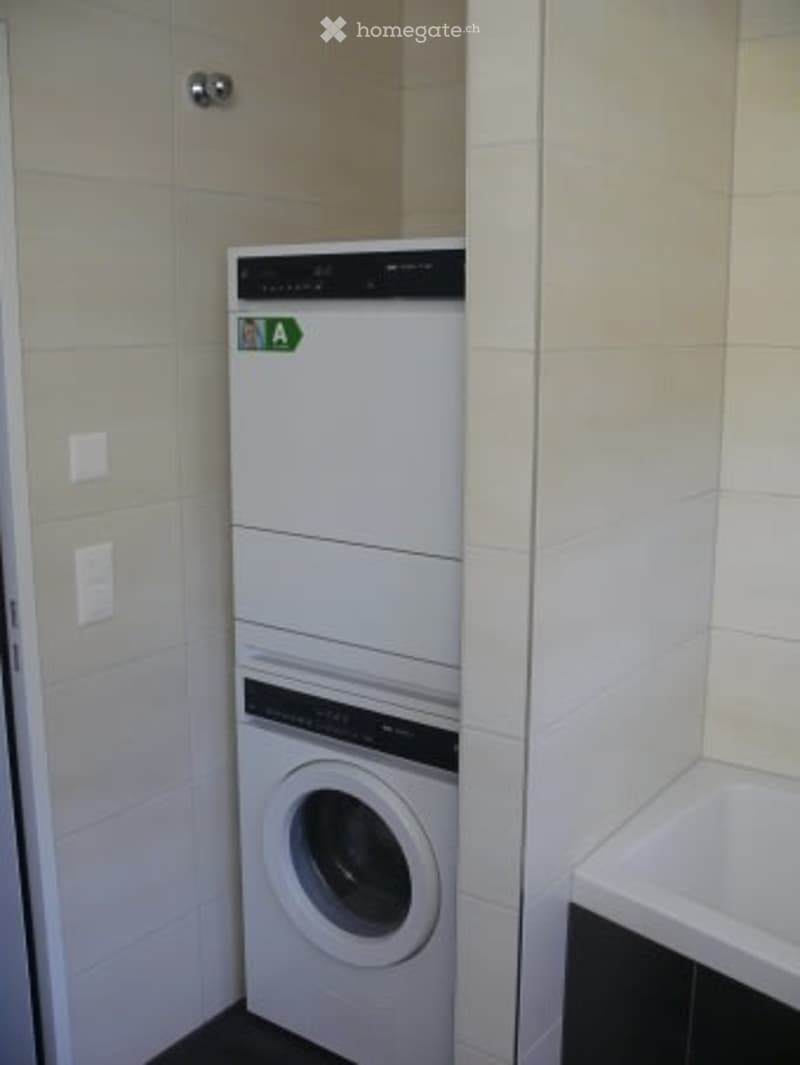 Bathroom with a white tiled wall, a washing machine, and a dishwasher installed side by side.