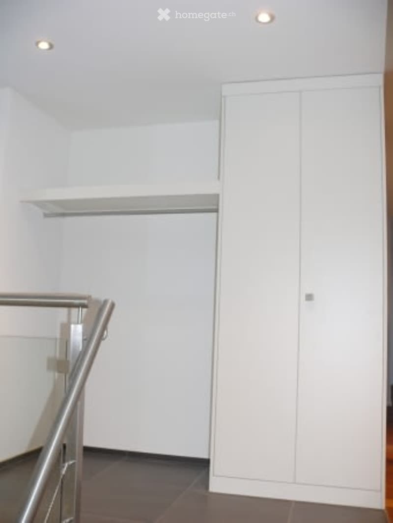 Empty room with white walls, a built-in closet, and a glass staircase railing.