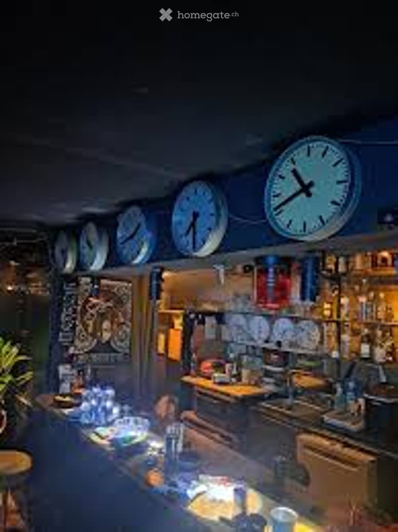A cozy kitchen with multiple clocks on the wall, a counter with cups and bottles, and a sink with a faucet.