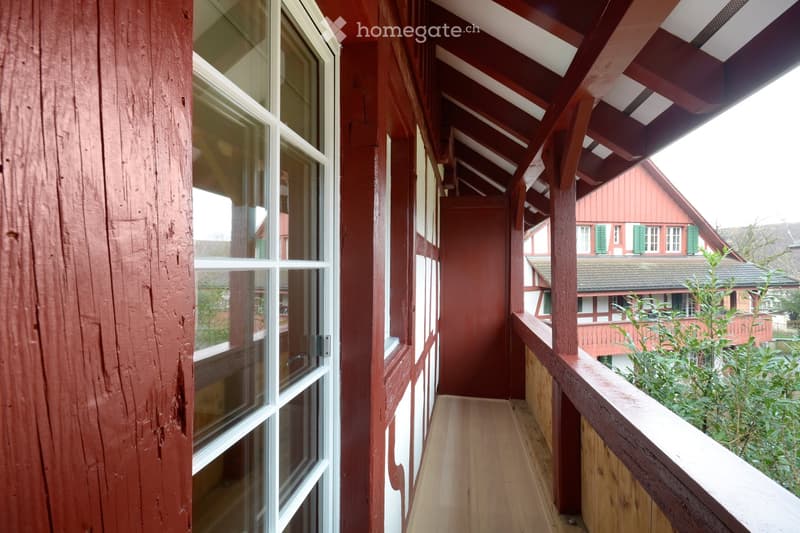 Wooden hallway with red wooden walls, large windows, and a wooden railing leading to an outdoor area.