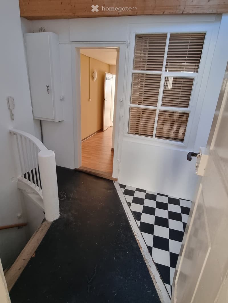 Entry hall with black and white checkered flooring, staircase, telephone, and doorways leading to different rooms.