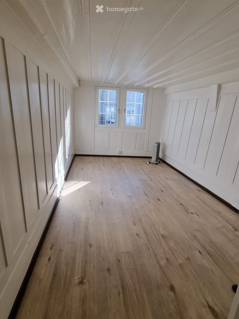 Empty room with white walls, wooden floor, and windows with white frames.