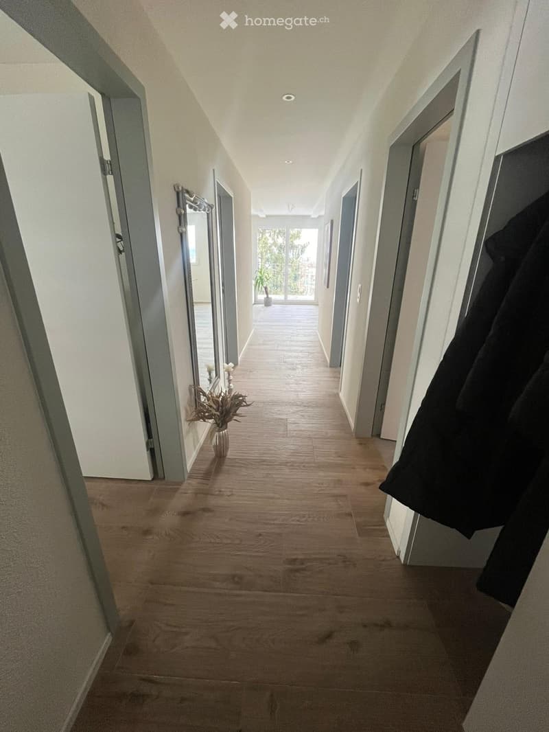 long hallway, wooden floor, white walls, mirror, vase with flowers, open door, glass door with plants