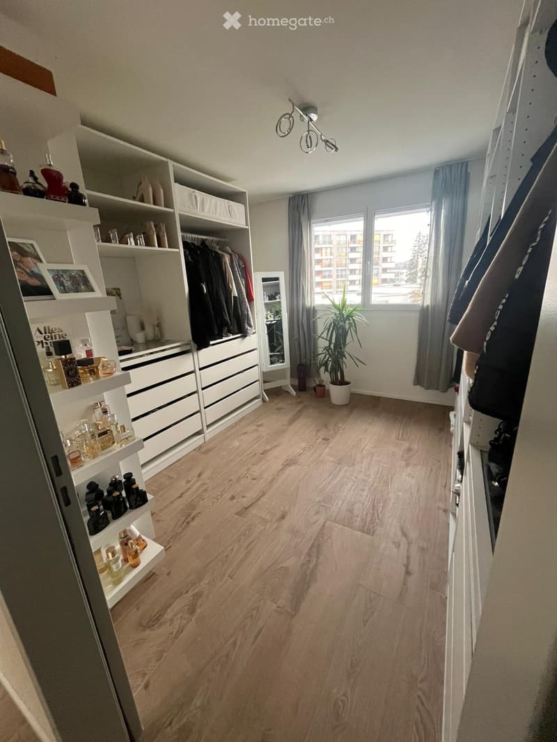 Large room with built-in wardrobes, floor lamps, white tiled floor, closet, and clothing racks, window with gray curtains