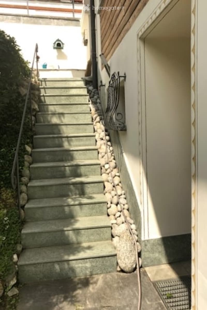 A narrow outdoor staircase leading up to a building entrance, bordered by a stone wall and metal railing.