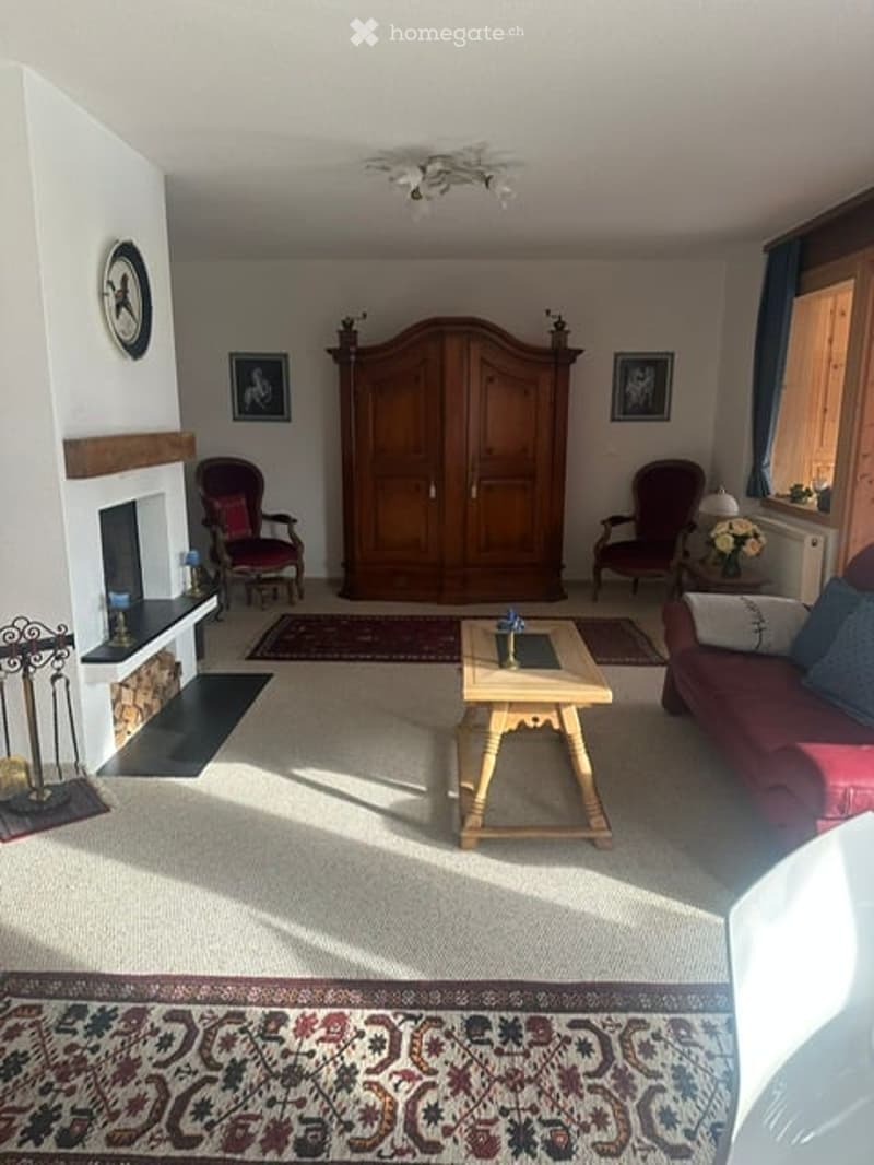 Bright living room with a fireplace, large wooden cabinet, red armchairs, a sofa, coffee table, and decorative items.