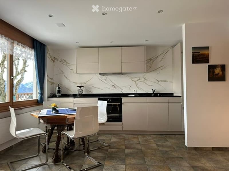 Modern kitchen with white cabinets, marble backsplash, and a dining area featuring a wooden table and white chairs.