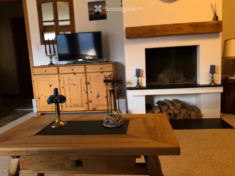 Living room with a wooden coffee table, television on a wooden cabinet, fireplace with stacked wood, and decorative candle holders.