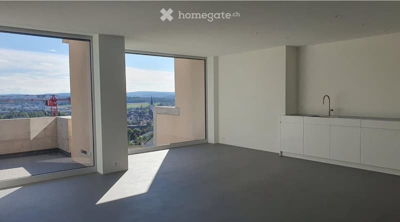 Modern, unfurnished room with large windows offering a scenic view, white cabinetry, and a sleek sink.