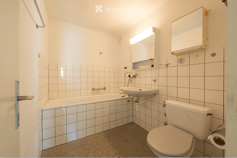Modern bathroom with white tiled walls and floor, featuring a bathtub, sink, toilet, and a mirror with built-in storage.