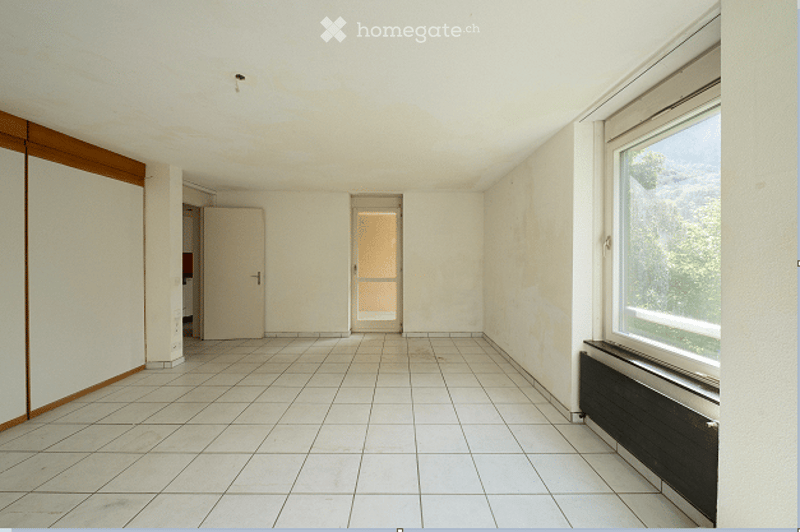 Empty room with white tiled floor, white walls, and large windows. No furniture or equipment present.