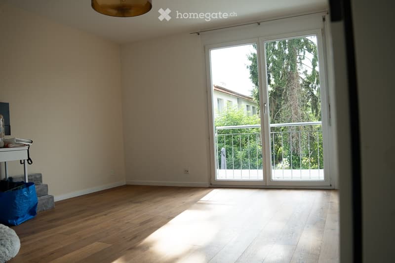Empty room with wooden flooring, large sliding glass door leading to a balcony, and minimal furnishings.