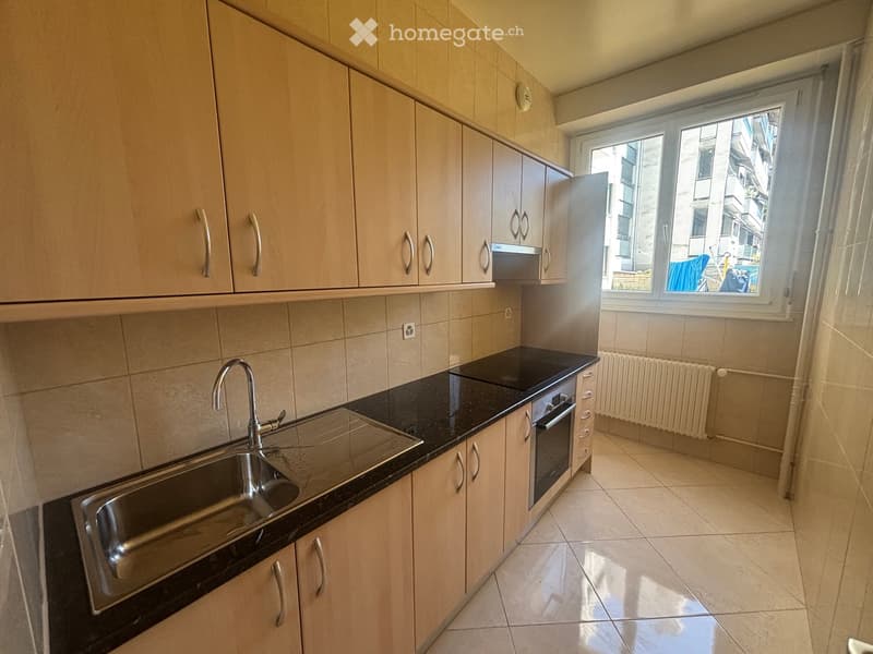 Modern kitchen with light wooden cabinets, black countertop, stainless steel sink, and built-in oven.