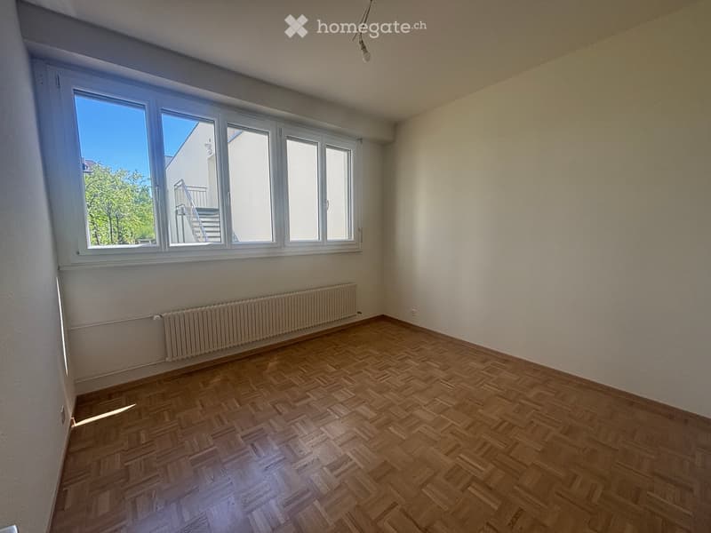 Empty room with wooden flooring, large windows, and a radiator under the windows.