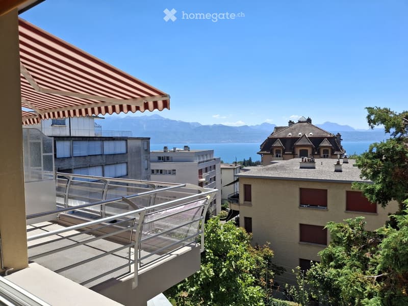 Balcony with a striped awning, metal railing, and scenic view of a lake and mountains.